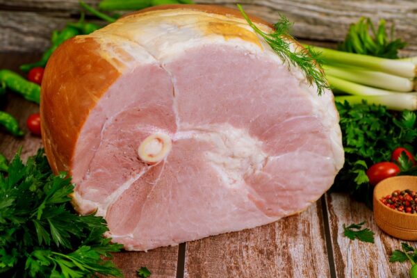 Smoked bone in ham with vegetables and spice on wooden Christmas table.