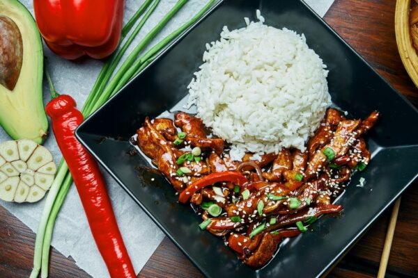 A classic Asian dish - rice with teriyaki fried pork wok in a black plate on a wooden background. Close up